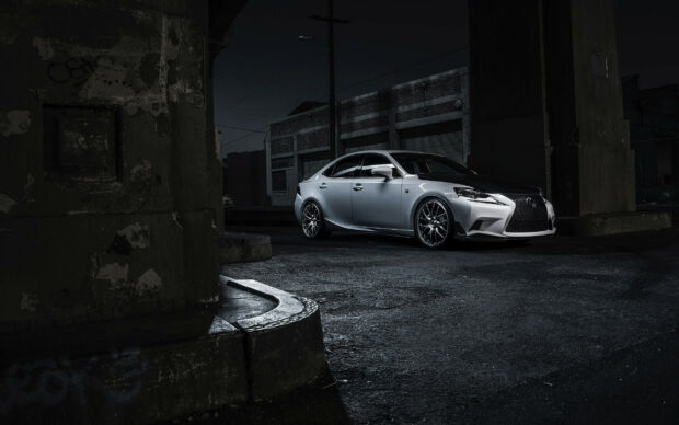 Silver Lexus parked in a dark urban street with old buildings around