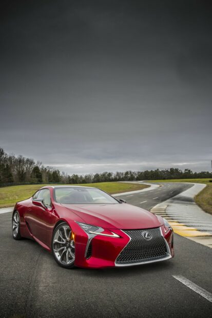 Red Lexus sports car on a curved road with a cloudy sky background