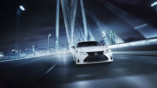 A white Lexus car driving on a futuristic bridge with city lights in the background