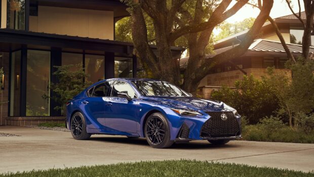 Blue Lexus sedan parked in front of a modern house surrounded by trees and greenery