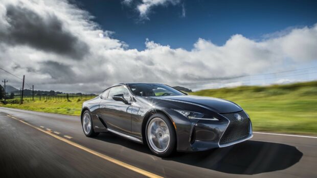 A sleek Lexus coupe driving fast on a countryside road under a cloudy sky