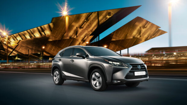A sleek Lexus NX driving past a modern architectural structure at night with vibrant city lights