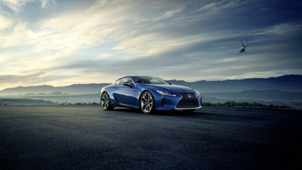 Blue Lexus car parked on open road with mountains and helicopter in background
