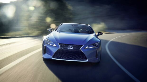 Blue Lexus driving on a winding road with sunlight reflecting on the car surface