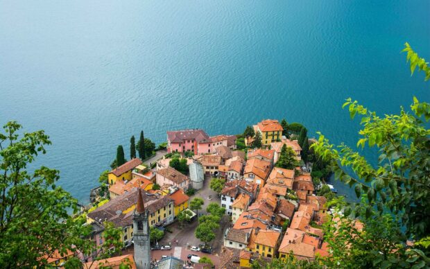Aerial view of a Lombardy town with colorful buildings near a large serene lake surrounded by greenery