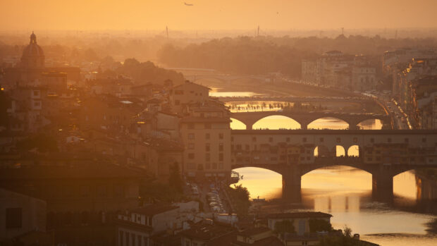 Historic Lombardy cityscape with bridges and river during golden hour haze