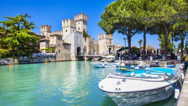 Historic Lombardy castle beside a turquoise lake with boats and green trees