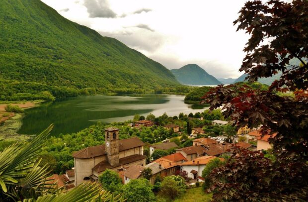 A scenic village with a clock tower near a calm lake surrounded by lush Lombardy hills