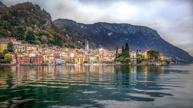 Colorful townscape in Lombardy reflected on the lake with mountain landscape in the background