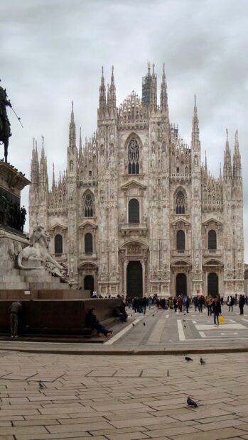 The historic Milan cathedral facade in Lombardy with intricate gothic details and people walking around