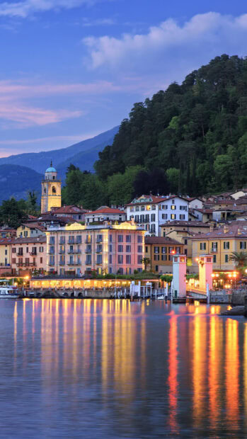 Evening reflections of Lombardy town with illuminated buildings and forested hills
