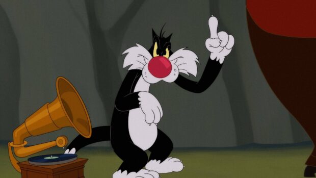 Sylvester the cat from Looney Tunes pointing upward near a gramophone in a cave setting