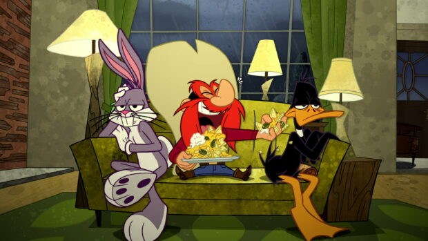 Bugs Bunny and Yosemite Sam enjoying snacks with Daffy Duck on a green couch in a cozy living room