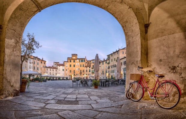 A red bicycle leaning against an old stone wall in Lucca Italy town square