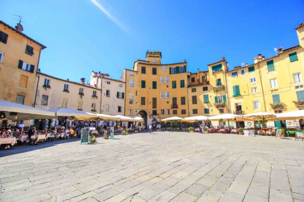 A vibrant Lucca city square with yellow buildings and outdoor cafes under a clear blue sky