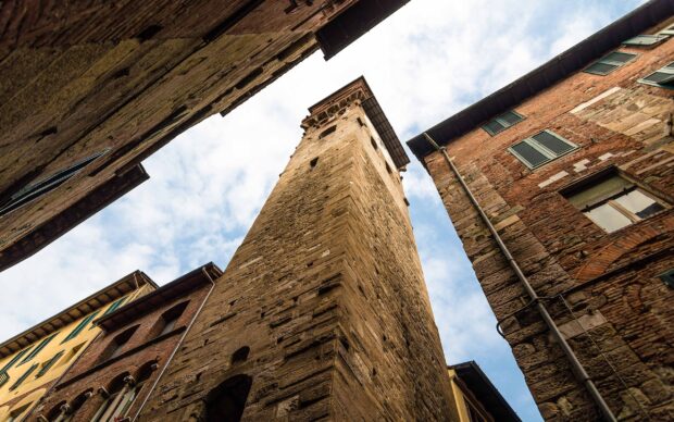 Historic architecture in Lucca Italy with towering ancient stone buildings against a partly cloudy sky