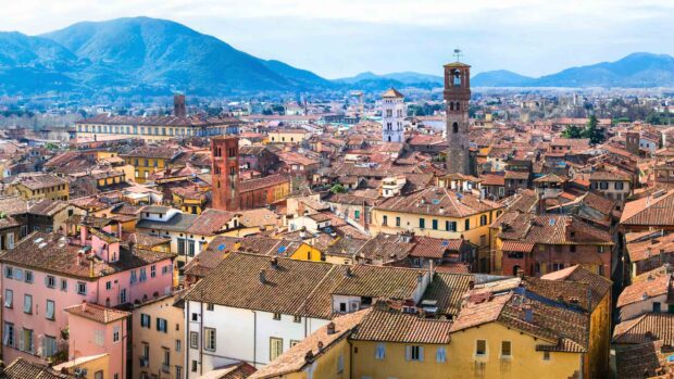 A panoramic view of Lucca Italy cityscape with historic towers and rooftops in the background of mountains