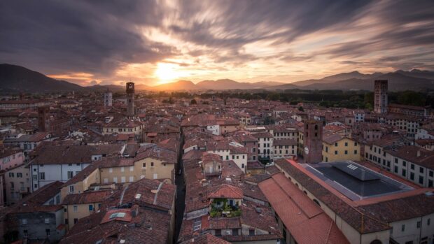 Ancient cityscape of Lucca Italy with terracotta rooftops at sunset showcasing historic towers and mountains