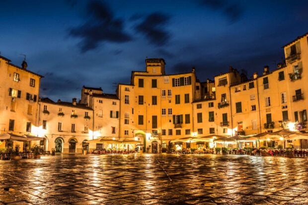 The historic center of Lucca Italy with illuminated buildings and wet cobblestone pavement at night