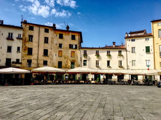 Historic buildings in Lucca Italy with outdoor umbrellas under a blue sky
