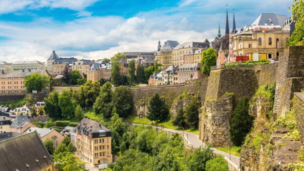 Historic Luxembourg cityscape with stone walls and lush greenery under a blue sky