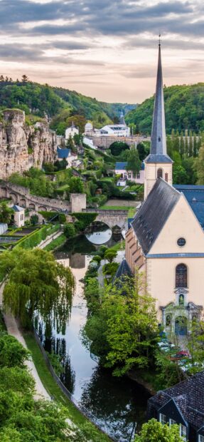 Historic Luxembourg cityscape with river and church steeple surrounded by greenery