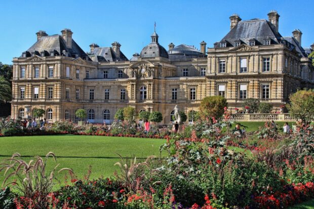 A historic Luxembourg building surrounded by lush green gardens and colorful flowers under a clear blue sky
