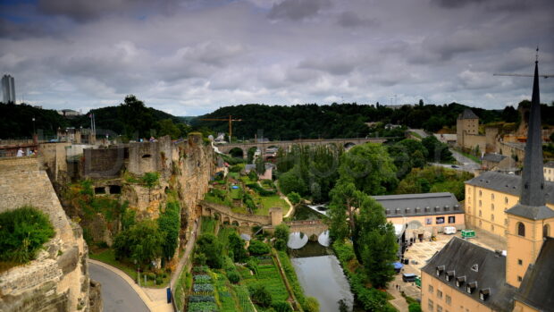 A scenic view of Luxembourg city with historic ruins and green landscape under cloudy sky