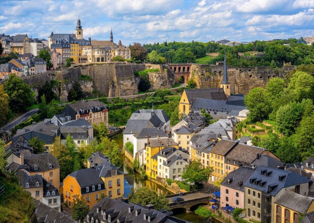 A beautiful cityscape of Luxembourg with historic buildings and lush greenery under a cloudy sky