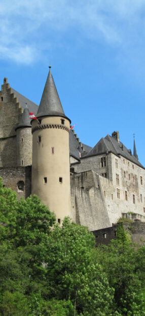 Ancient Luxembourg castle tower surrounded by lush green trees under blue sky