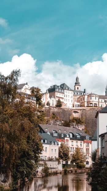 Historic buildings by the river in Luxembourg with autumn trees and a bright sky