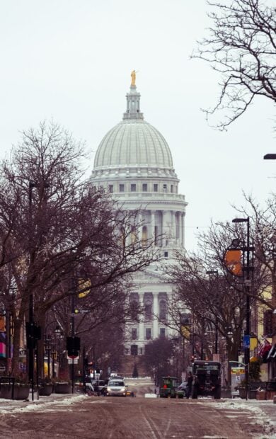 The capitol building of Madison Wisconsin stands tall among leafless trees along the city street in winter