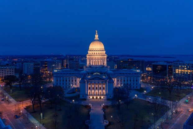 The historic state capitol in Madison Wisconsin illuminated at night with city lights in the background