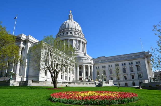The Madison Wisconsin capitol building with colorful tulips and green lawn in front on a clear sunny day