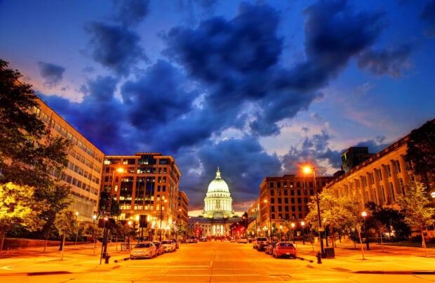 The capitol building in Madison Wisconsin stands between city streets and illuminated buildings at dusk