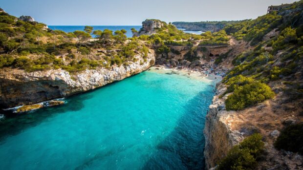 Crystal clear turquoise water in Mallorca rocky coast with pine trees and hidden beach