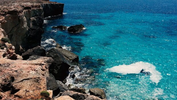 Rocky coast of Mallorca with clear blue sea waves crashing against the shore