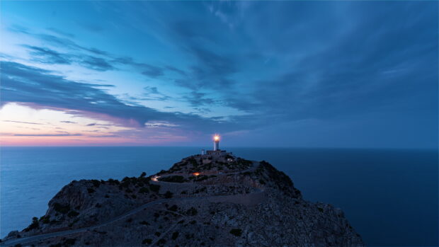 A lighthouse on a rocky cliff in Mallorca guides ships during twilight