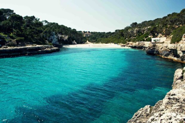 Clear turquoise waters surround the Mallorca coastline with rocky cliffs and lush greenery