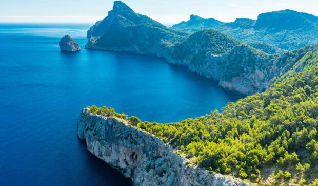 Rocky coastline and lush green forest at Mallorca coast in clear blue sea