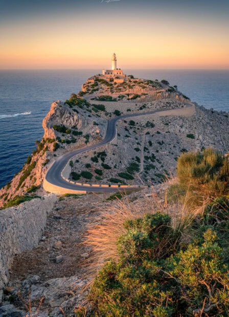 A winding road leading to a lighthouse on a rocky cape in Mallorca at sunset