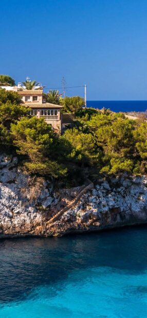 Beautiful Mallorca coastline with rocky cliffs and lush greenery above clear blue water