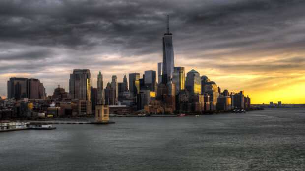 Dramatic Manhattan skyline at sunset with cloudy sky and glowing golden reflections