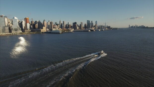 A boat moving across the water near Manhattan skyline at sunset
