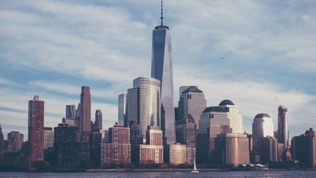 Manhattan city skyline with tall skyscrapers and a sailboat in the water at sunset