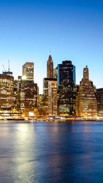 Evening cityscape of Manhattan with illuminated buildings and calm water reflecting lights