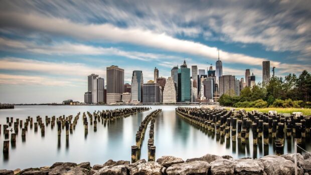 Old wooden pier leading to Manhattan skyline under cloudy sky