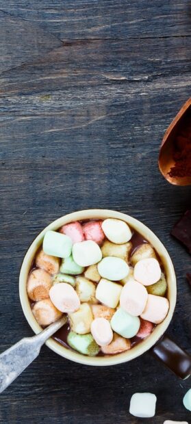 A bowl filled with colorful marshmallow floating in hot chocolate on a wooden table