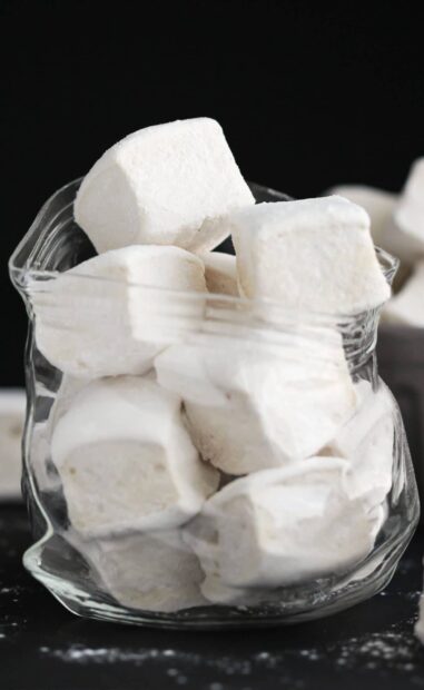 Soft marshmallow cubes stacked in a clear glass jar against a dark background