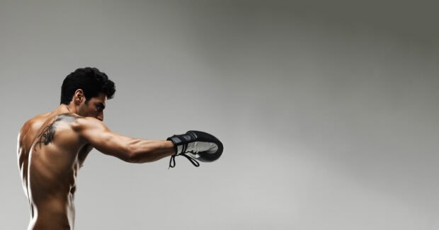 Muscular man practicing martial art punching with boxing gloves and tattoo on back